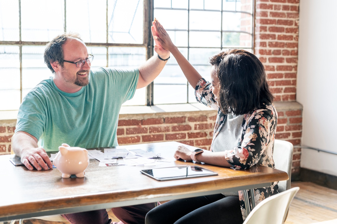 two people high-fiving in a meeting room with a piggy bank