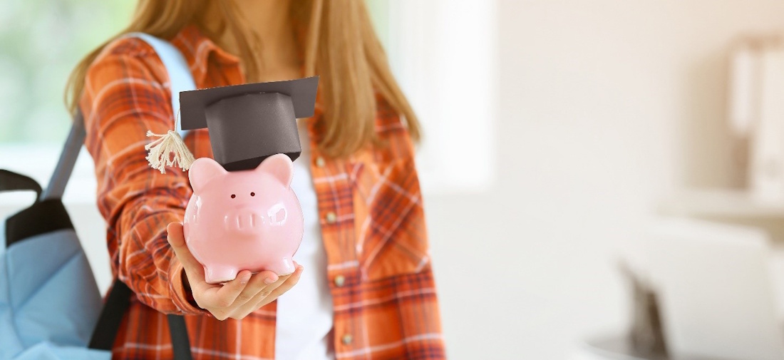 young woman holding out a piggy bank with a graduation cap on it