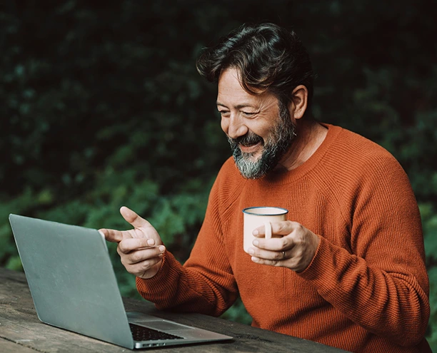 Adult sitting outdoors holding a mug and using a laptop